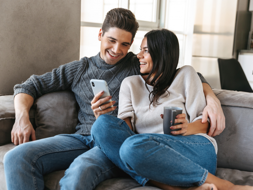 man and woman sitting on a couch looking at phone